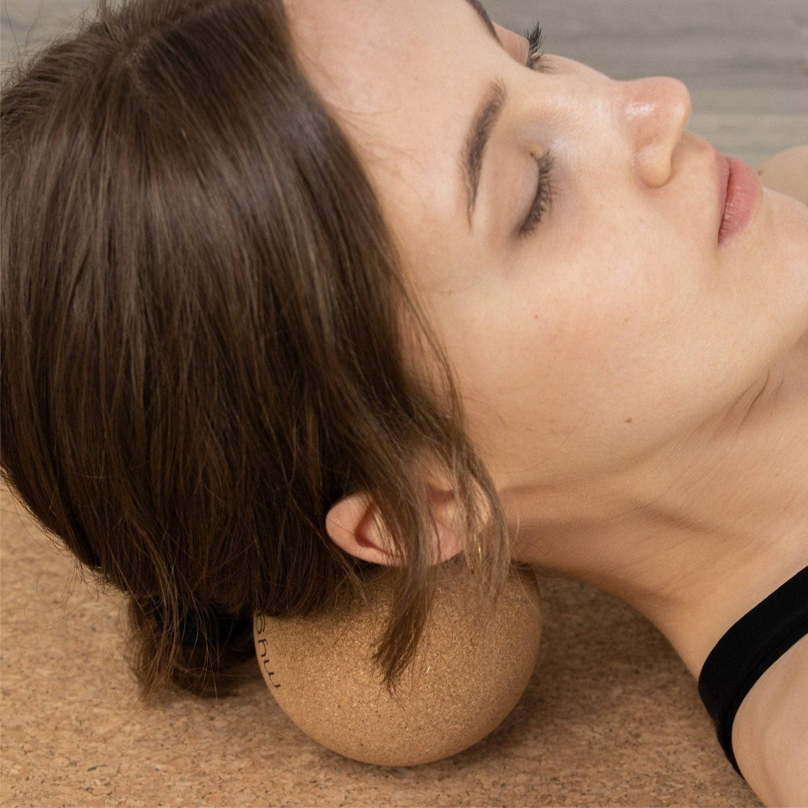 Woman lying down using a cork massage ball beneath the back of her neck